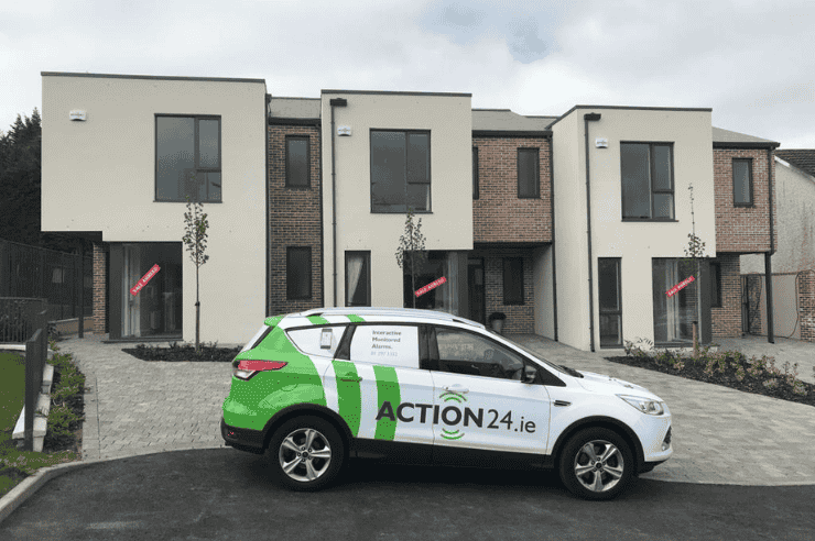 Action24-branded vehicle parked on the street in front of a row of three houses