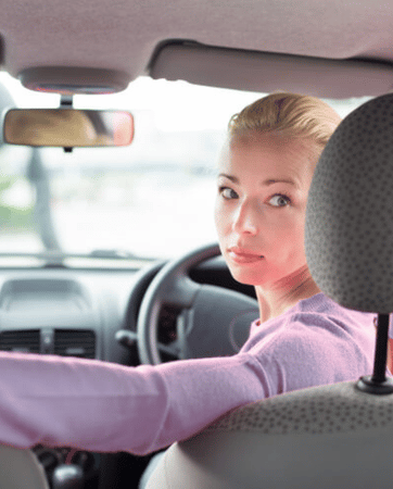 Interior view of a car, woman seen from behind, looking over her shoulder, reverse parking