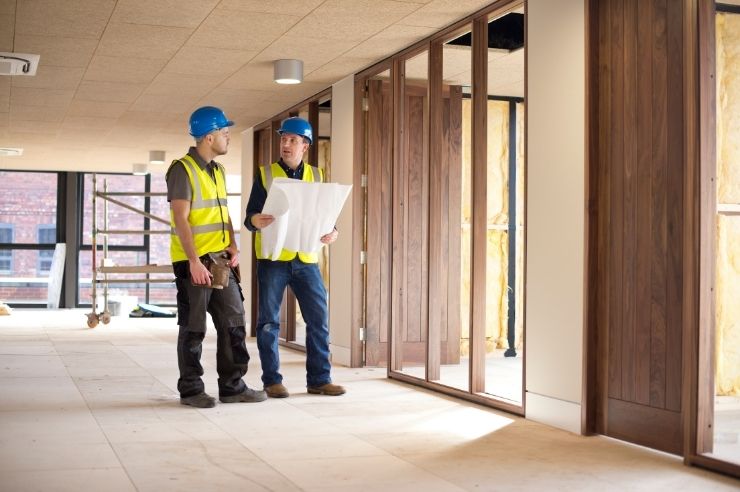 2 men looking at plans for old house Two builders working on-site, wearing hard hats and reviewing documents
