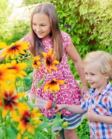 2 kids watering the flowers in the garden