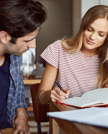 Couple sitting at a table reviewing notes and paperwork beside a laptop.