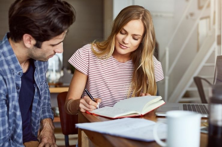 Couple sitting at a table reviewing notes and paperwork beside a laptop.