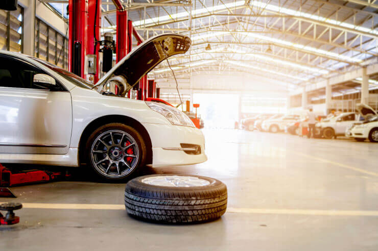 White car in large garage, the hood is open and a wheel lays next to it