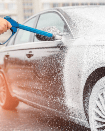 Black car covered in soap, being washed with blue power washer