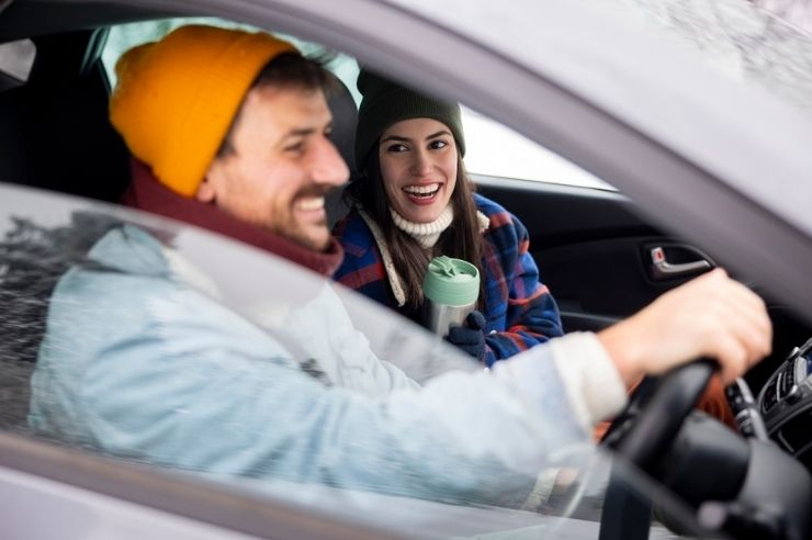 Man driving a car with a woman in the passenger seat holding a travel mug.