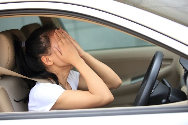 Woman at steering wheel, looking frustrated with both hands covering her face