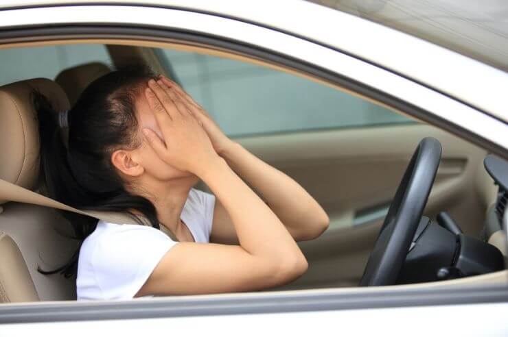 Woman at steering wheel, looking frustrated with both hands covering her face