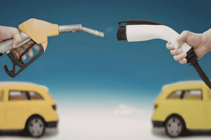 •	A hand holding a fuel pump across from another hand holding an electric car charger