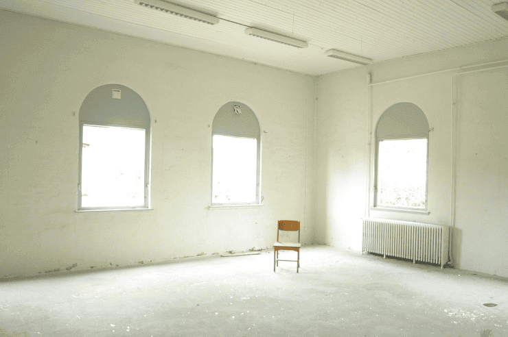 Wide, empty room with three bright windows and a wooden chair
