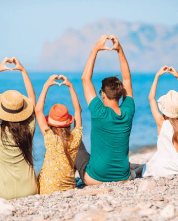 Photo of family with back to camera on a beach making hearts with their hands