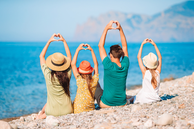 Photo of family with back to camera on a beach making hearts with their hands