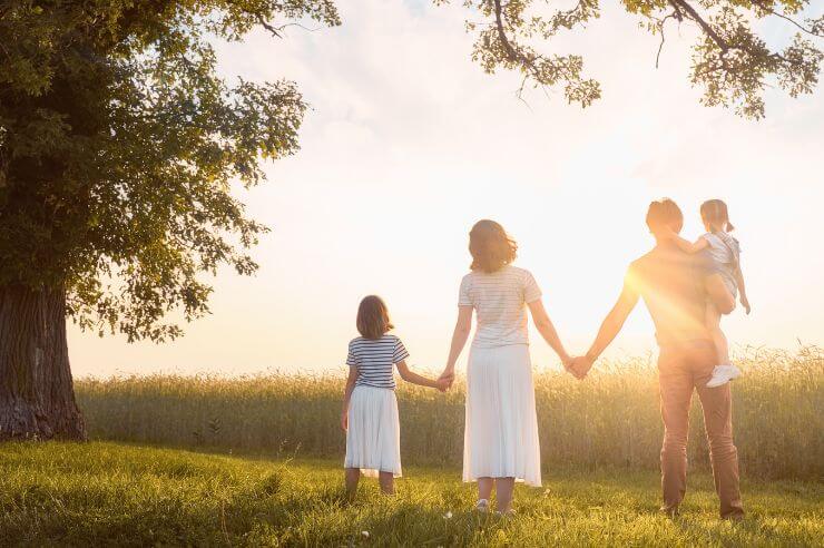 Family walking in the fields in the sunshine Family of four with two children holding hands in the sunshine