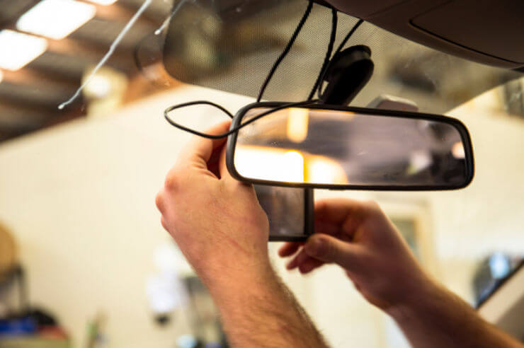 Photo of driver adjusting their dashcam with rearview mirror and windshield visible.