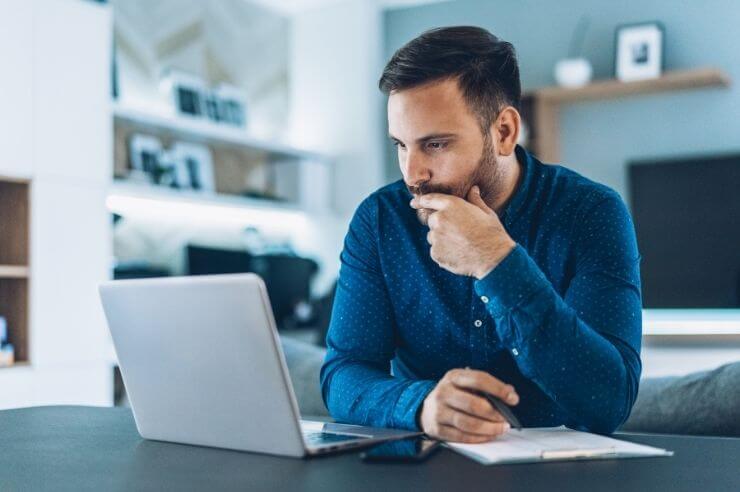 Man at desk with his laptop, he has a notepad in pen with him
