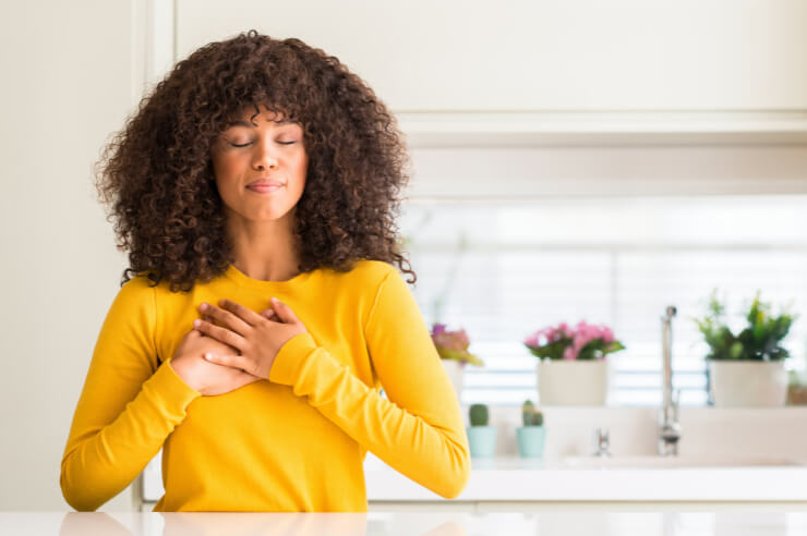 Woman standing at kitchen counter, hands clasped at her chest with her eyes closed