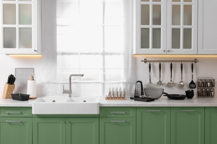Fitted kitchen with green lower cabinets, white glass-fronted wall units and a double sink.