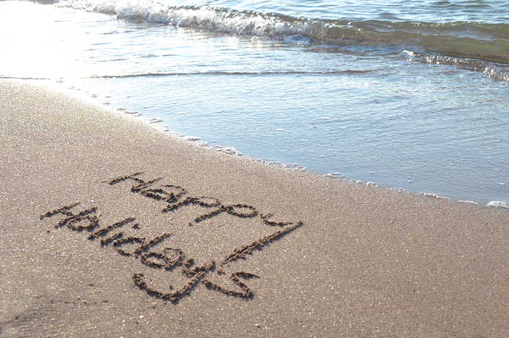 Happy holidays written on the sand on a beach
