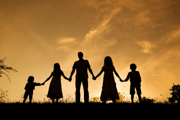 Family of five, seen from behind, holding hands facing the sunset