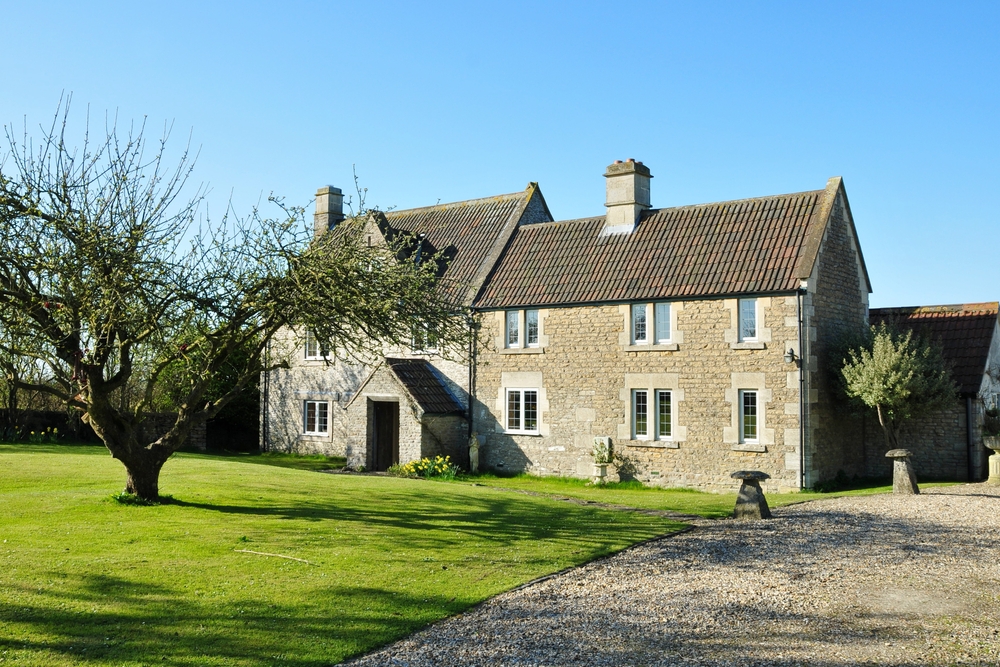 Detached period stone farmhouse with a tiled roof, set on a lawn beside a gravel drive.