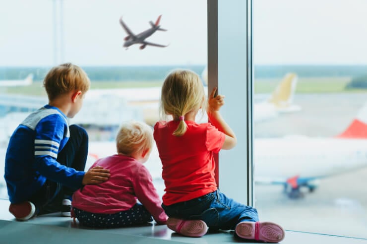 Three children looking out the window of an airport watching planes depart