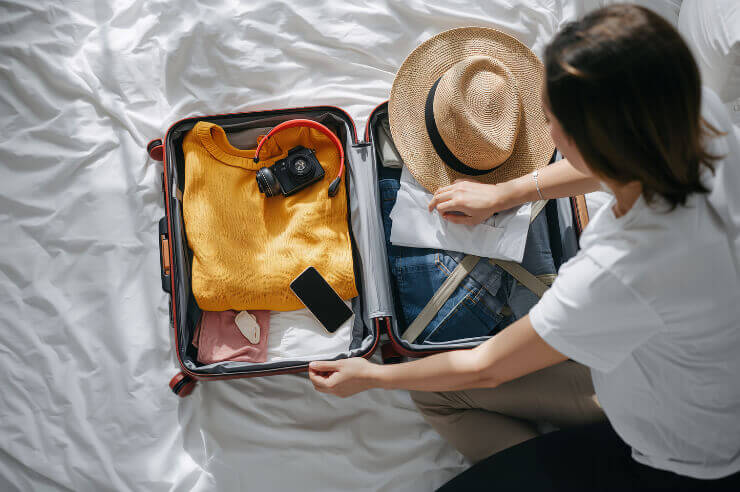 Woman packing a carry on suitcase containing a camera, hat and clothes