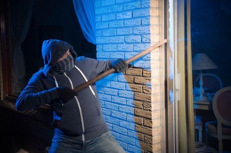 Burglar wearing a hoodie and mouth covering attempting break in through a sliding door