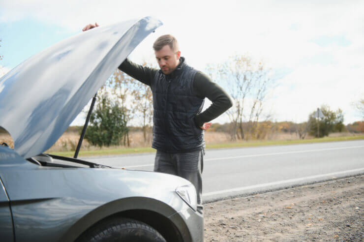 Man checking under the hood of car pulled in at the side of the road