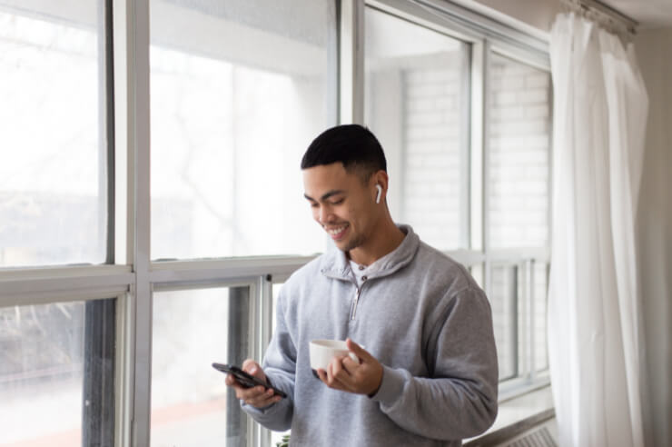 Man standing near windows holding phone and holding a mug