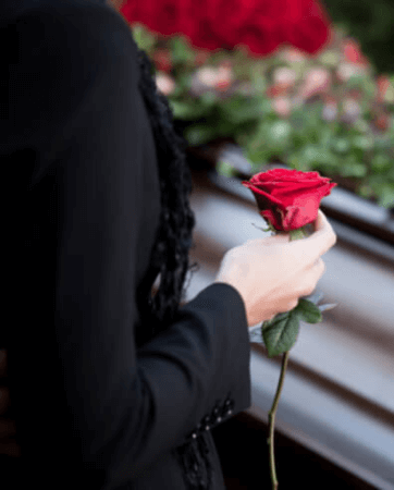 Woman standing over coffing holding a red rose