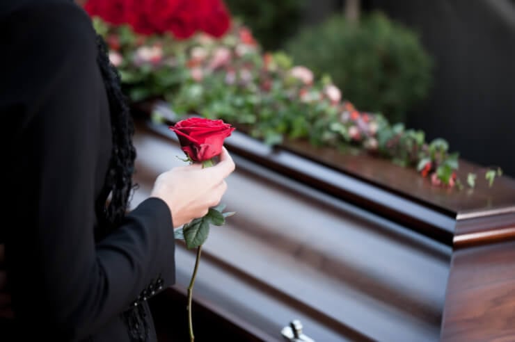 Woman standing over coffing holding a red rose