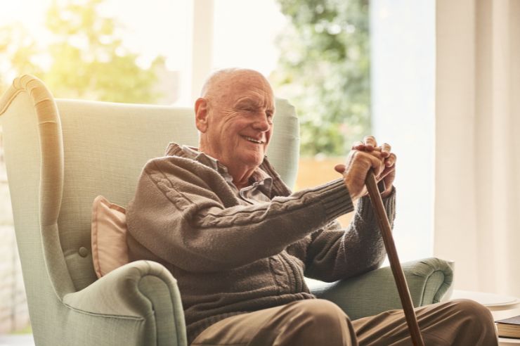 Elderly man with cane sitting in a chair smiling