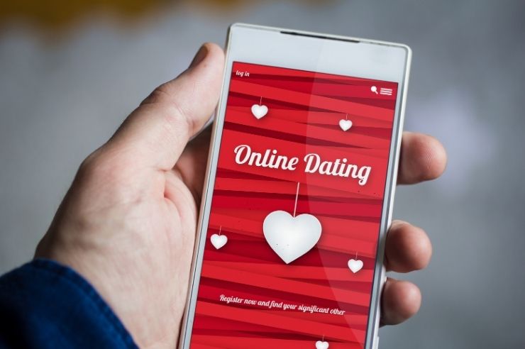 White smartphone in a man's hand, the screen shows an online dating application