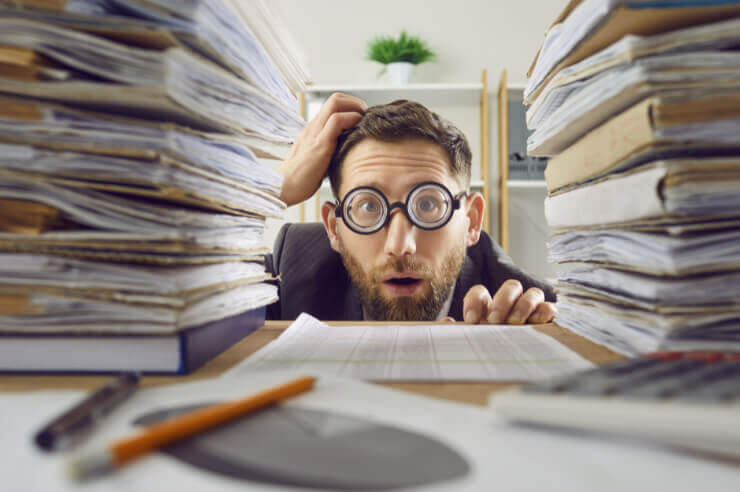 Man wearing glasses looking confused between two large stacks of documents