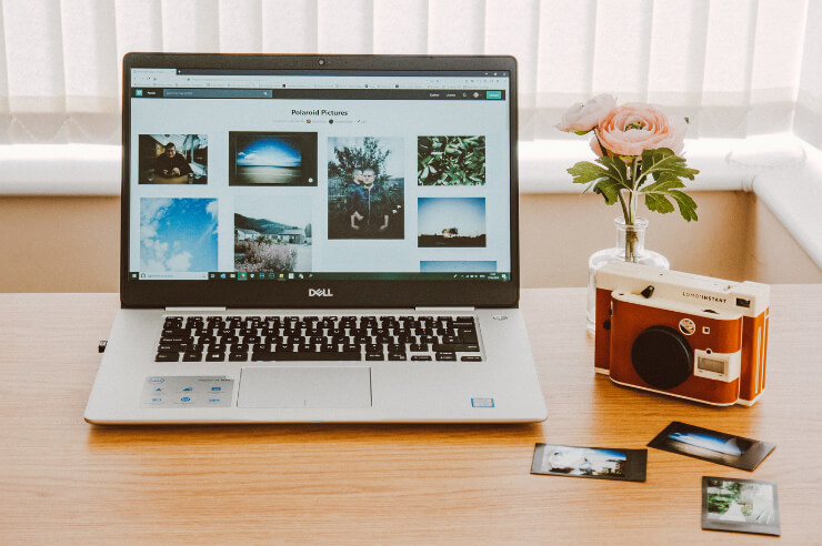 Laptop on desk with images on screen, a camera next to it with printed photos