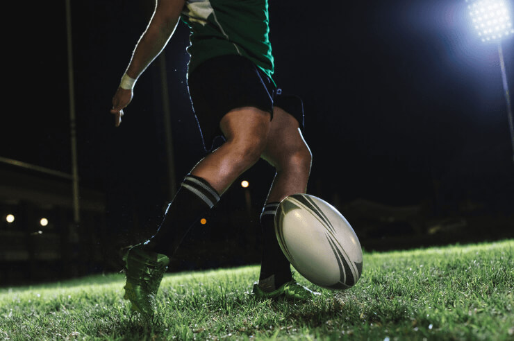 Rugby player playing rugby at night time Rugby player on the pitch at nighttime about to kick the ball