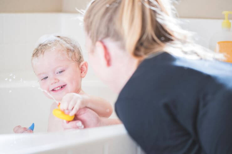 Child sitting in bathtub with older woman observing