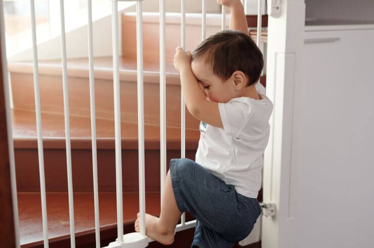 Toddler climbing white safety gate equipped to staircase