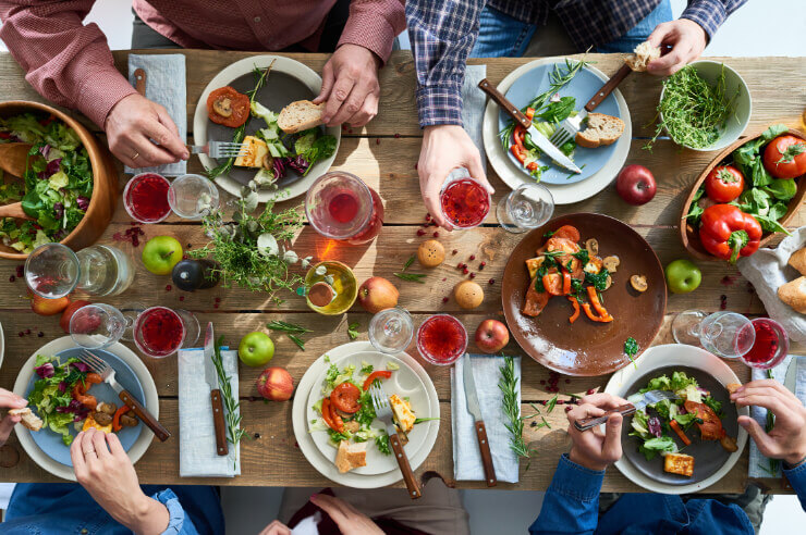 Top down view of table with people sat around eating colourful fruits, vegetables and salads