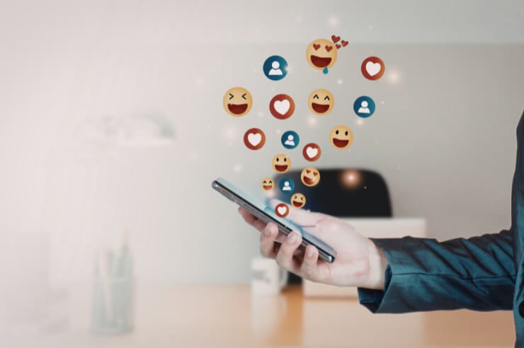 Person holding a mobile phone, reaction emojis float above it