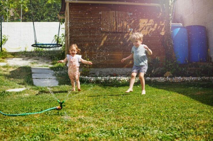 Kids running in the garden playing with a water sprinkler Two toddlers playing with a water sprinkler