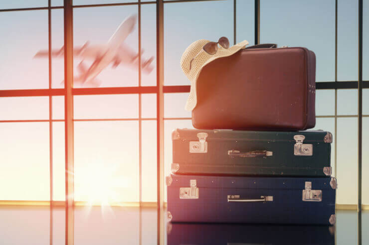 Suitcases stacked with a hat and sunglasses on top, the sun sets in the background