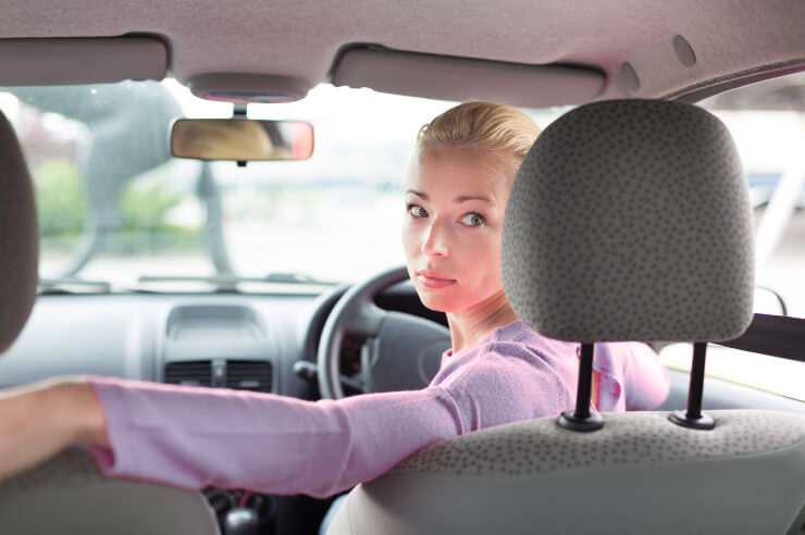 Interior view of a car, woman seen from behind, looking over her shoulder, reverse parking 