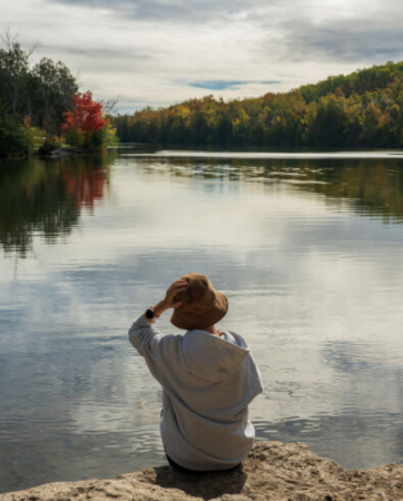 Woman sitting alone at lake wearing a hat