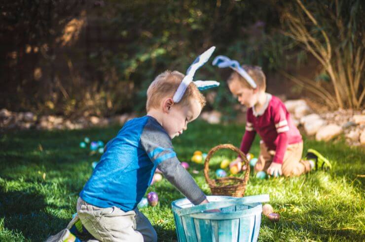 young boys collecting easter eggs wearing bunny ears Two children wearing rabbit ears sitting in green field collecting colourful eggs