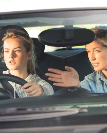 Young lady driving a car with an older lady teaching her