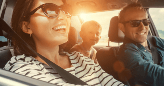 Smiling family driving together in a car on a sunny day.