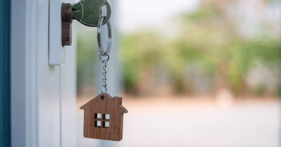 Close-up of a house key in a door lock with a wooden house-shaped keychain.