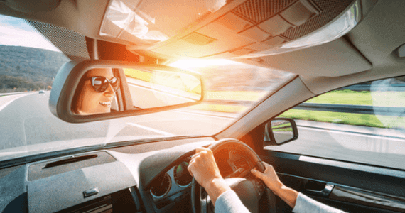 A woman driving confidently on a sunny day, reflected smiling in the rear-view mirror.