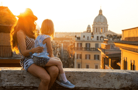 Woman and child sitting on a wall, enjoying a scenic city view at sunset.