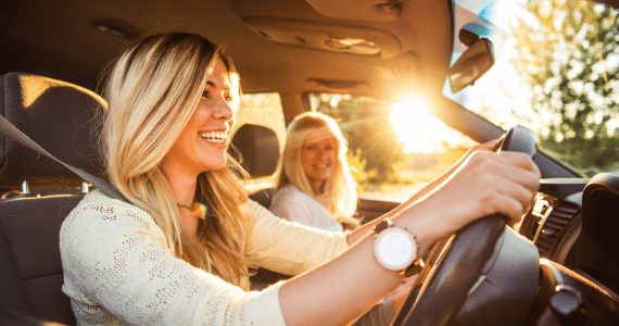 Two smiling women in a car during golden hour, with the driver enjoying the ride.